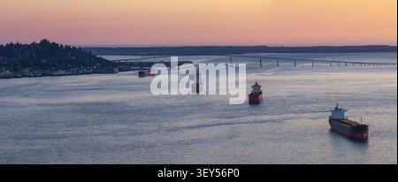 Aerial view of the Columbia River with cargo ships navigating the waterway near the Astoria-Megler Bridge at sunset in Astoria, Oregon, United States. Stock Photo