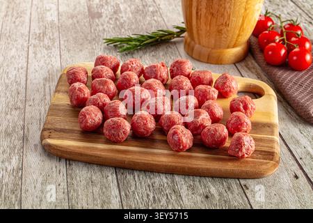 Fresh raw meatballs arranged on rustic wooden board. Cherry tomatoes rosemary sprig add color contrast. Warm natural lighting enhances red meat tones Stock Photo
