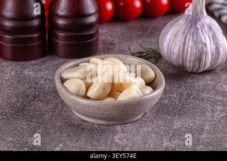 Garlic cloves arranged in speckled ceramic bowl on textured gray surface. Whole garlic bulb red tomatoes in soft focus background Stock Photo