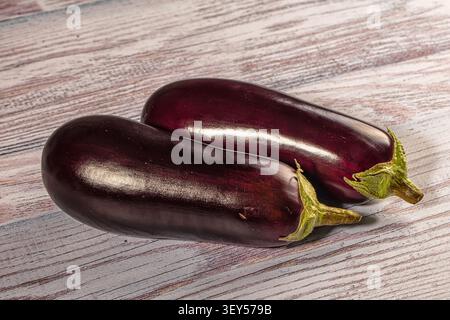 Two fresh eggplants with deep purple skin green stems rest on weathered wood. Soft lighting highlights glossy texture. Natural composition with earthy Stock Photo