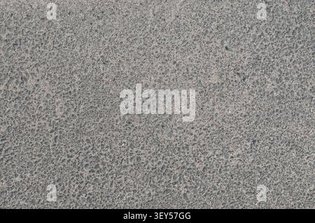 A detailed close-up view of a gray asphalt surface showing a rough, uneven texture with various small stones and gravel pieces. Stock Photo