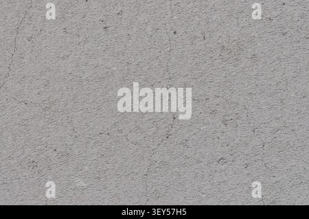 A close-up view of a weathered, gray concrete wall showing fine cracks and a coarse, grainy texture. The surface is uneven and shows signs of aging. Stock Photo