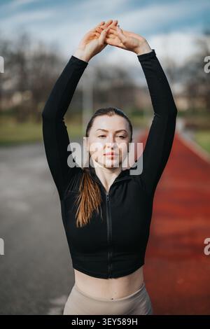 Fit woman stretching arms overhead on outdoor running track during morning workout session Stock Photo