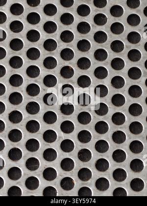 Close up view of worn silver metal surface with evenly spaced round holes, showing repeating geometric pattern, rough scratches, and dark openings tha Stock Photo