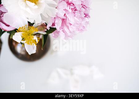 Pink peonies and white flower petals arrange in glass vase on white table. Flower card with copy space, minimalist floral background banner, elegant Stock Photo