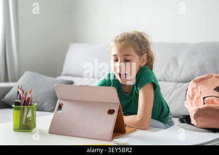 Happy elementary school girl using a digital tablet while studying at home. Stock Photo