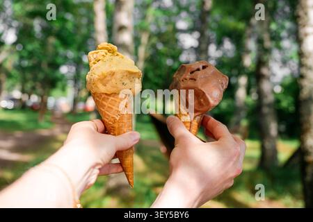 Two hands holding colorful ice cream cones with chocolate and pistachio scoops in sunny summer park Stock Photo