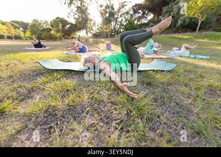 Seniors doing yoga and pilates exercises on mats in park Stock Photo