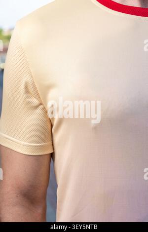 Close-up of a young male athlete wearing a beige sports jersey with red collar and breathable mesh panels on the shoulder. Outdoor natural light, shal Stock Photo