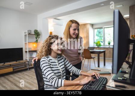 Two women are seated in front of a computer monitor, focusing on the screen as they engage in work or discussion. They appear to be deep in concentration, possibly collaborating on a project or analyzing data. Stock Photo