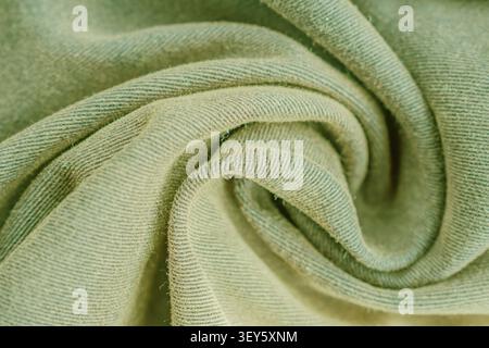 Horizontal close up macro shot of a soft olive green cotton fabric texture folded in a spiral shape with detailed diagonal weave pattern under soft li Stock Photo