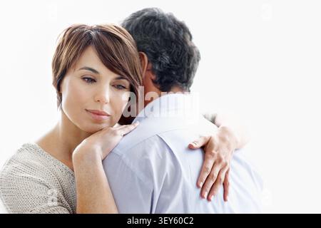 Couple, hug and thinking with love in studio for comfort or commitment on a white background. Man, embrace and thoughtful woman with gentle touch or Stock Photo