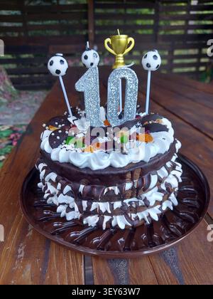 A beautifully decorated chocolate cake adorned with whipped cream and candies, set on a wooden surface, possibly an outdoor table, creating a celebratory atmosphere with a top-down view ofa. Stock Photo