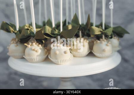 Elegant dessert treats adorned with green bows. White cake pops sit on a minimalist stand. Each pop features delicate pearl-like toppings. Green ribbo Stock Photo