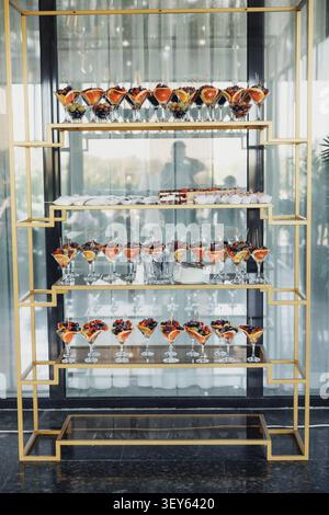 Elegant glasses hold colorful cocktails on gold-framed shelves. Shelves reflect light, enhancing sophistication of display. Glassware gleams against p Stock Photo