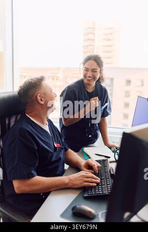 Happy male and female doctors laughing while working on computer at hospital Stock Photo