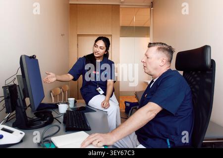 Multiracial healthcare professionals reviewing data over computer while sitting in clinic office Stock Photo