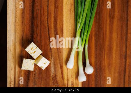 A top-down photograph showing three neat cubes of white feta cheese on the left and a cluster of fresh green spring onions (scallions) with water drop Stock Photo