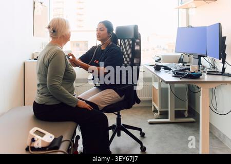 Female healthcare professional using stethoscope to check senior patient's heartbeat Stock Photo
