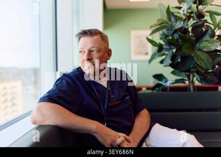 Thoughtful male healthcare professional looking out of window while relaxing on sofa Stock Photo
