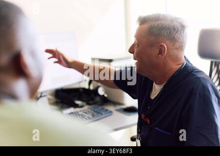 Male healthcare professional explaining medical reports to patient over computer screen Stock Photo