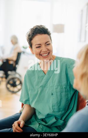 Happy female nurse having conversation with senior woman at retirement home Stock Photo