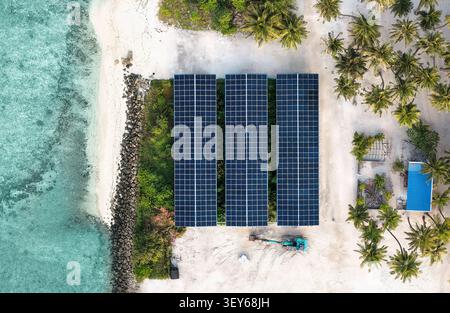 Aerial view of solar panels installed on a sandy beach near turquoise waters, surrounded by palm trees and a small excavator in Vaikaradhoo, Haa Dhaal Stock Photo