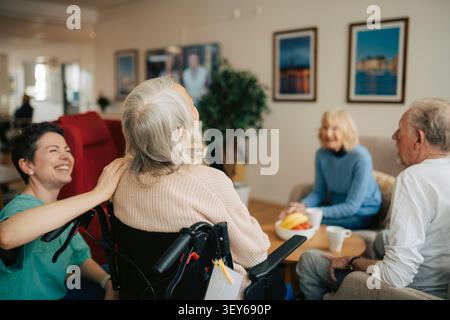 Happy female nurse spending leisure time with senior people at retirement home Stock Photo