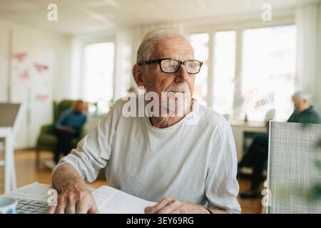 Thoughtful senior man looking away while sitting at table with book Stock Photo