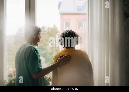 Smiling female nurse next to senior woman looking out of window Stock Photo