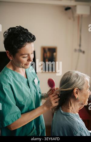 Female nurse tying hair of senior woman at nursing home Stock Photo