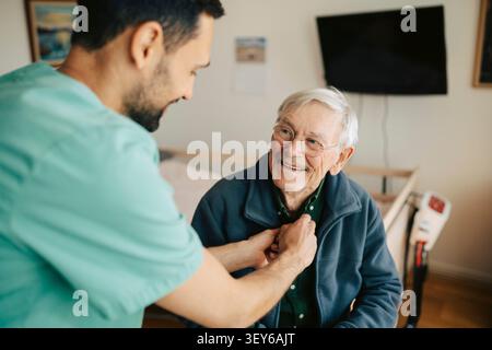 Male nurse helping senior man to dress up at nursing home Stock Photo