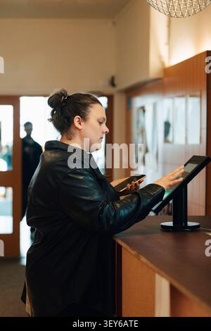Female freelance worker using touch screen kiosk to check in at modern coworking office Stock Photo