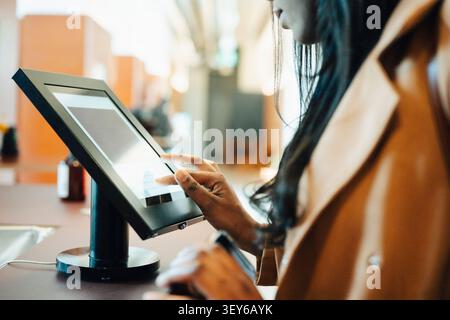 Close-up shot of female entrepreneur using touch screen kiosk at shared workspace front desk Stock Photo