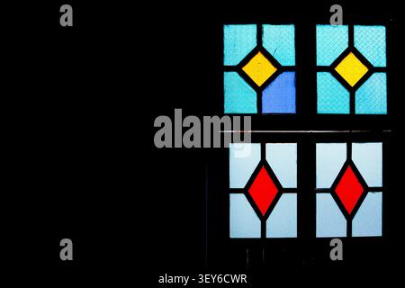 A striking minimalist shot of a traditional stained glass window set against a deep black shadow. Stock Photo