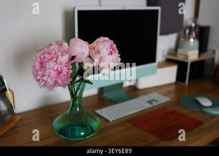 Cozy home office interior with floral decoration, modern desktop computer and smartphone on a minimalist wooden workspace. Stock Photo