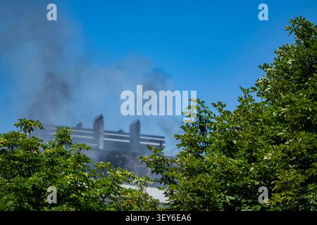 Large plume of black smoke rising over modern city buildings after an urban fire. Concept of emergency, environmental pollution, disaster, industrial Stock Photo