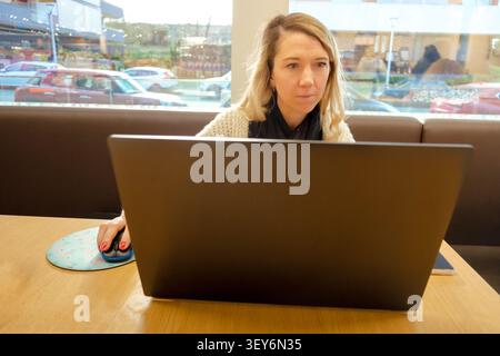Woman focusing on work using a laptop and mouse in a modern coffee shop environment Stock Photo