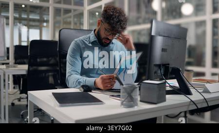 Arabian business man analyzing papers data stats diagram writing notes focused working employer write analyze finance at office ethnic businessman Stock Photo