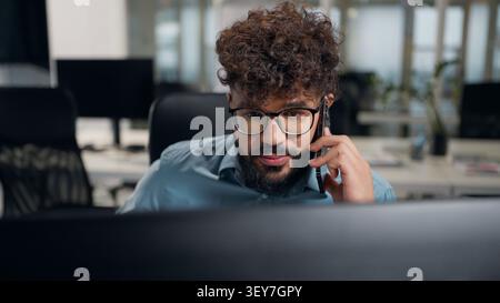 Arabian business man looking at computer monitor talking mobile phone at office ethnic businessman focused look in pc screen talk smartphone Stock Photo