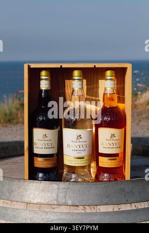 Three bottles of Banyuls in a wooden box on a barrel, with the coastline in the background. The Cap Cerbere Lighthouse is the last French lighthouse before the French-Spanish border; it is also known as the solar lighthouse. Vermeille Coast, the southernmost port on mainland France, just across the border from Spain. History, details, and architecture. France, Cerbere, June 28, 2026. Photo by Patricia Huchot-Boissier/ABACAPRESS.COM Stock Photo
