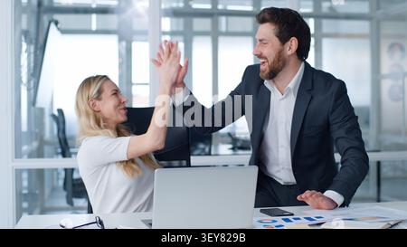 Business team two happy winners businesspeople workers winning with laptop giving high five in company Caucasian businesswoman with businessman win Stock Photo