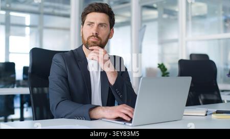 Concentrated dreamy Caucasian middle-aged business man thinking work solution focused looking away job decision mature businessman working with laptop Stock Photo