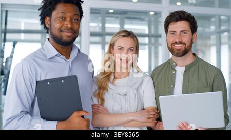Multiethnic business group three colleagues looking at camera smiling happy in company office project team African and Caucasian businessmen with Stock Photo