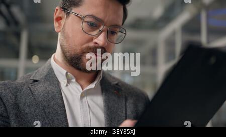 Serious Caucasian business man in glasses holding tablet with papers analyzing diagram income stats taxes data businessman middle-aged male specialist Stock Photo
