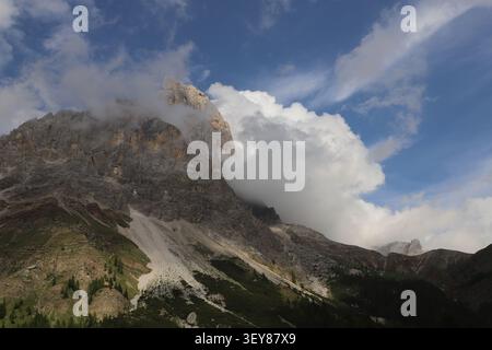 Massive rocky Dolomite mountain peak disappearing into low clouds above dense alpine forest in northern Italy. Stock Photo