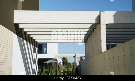 Modern concrete pergola creating striped shadow patterns on building facade under clear blue sky Stock Photo