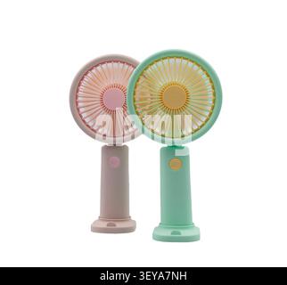 Two portable handheld fans in pastel pink and green on a white background, for cooling off on hot summer days. Stock Photo