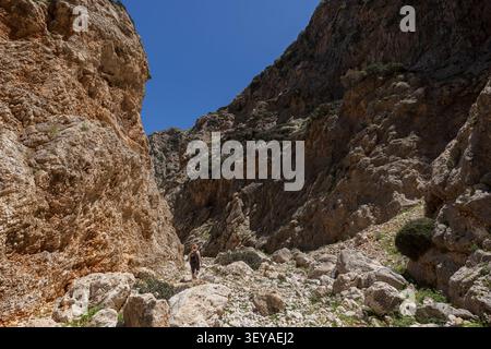 A woman hiking at the stunning Katholiko (or Avlaki) Gorge which features tall, steep, rugged and rocky cliffs, on a sunny day in Crete, Greece. Stock Photo
