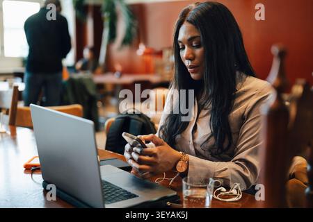 Female entrepreneur text messaging through smart phone during her work session at shared workspace Stock Photo